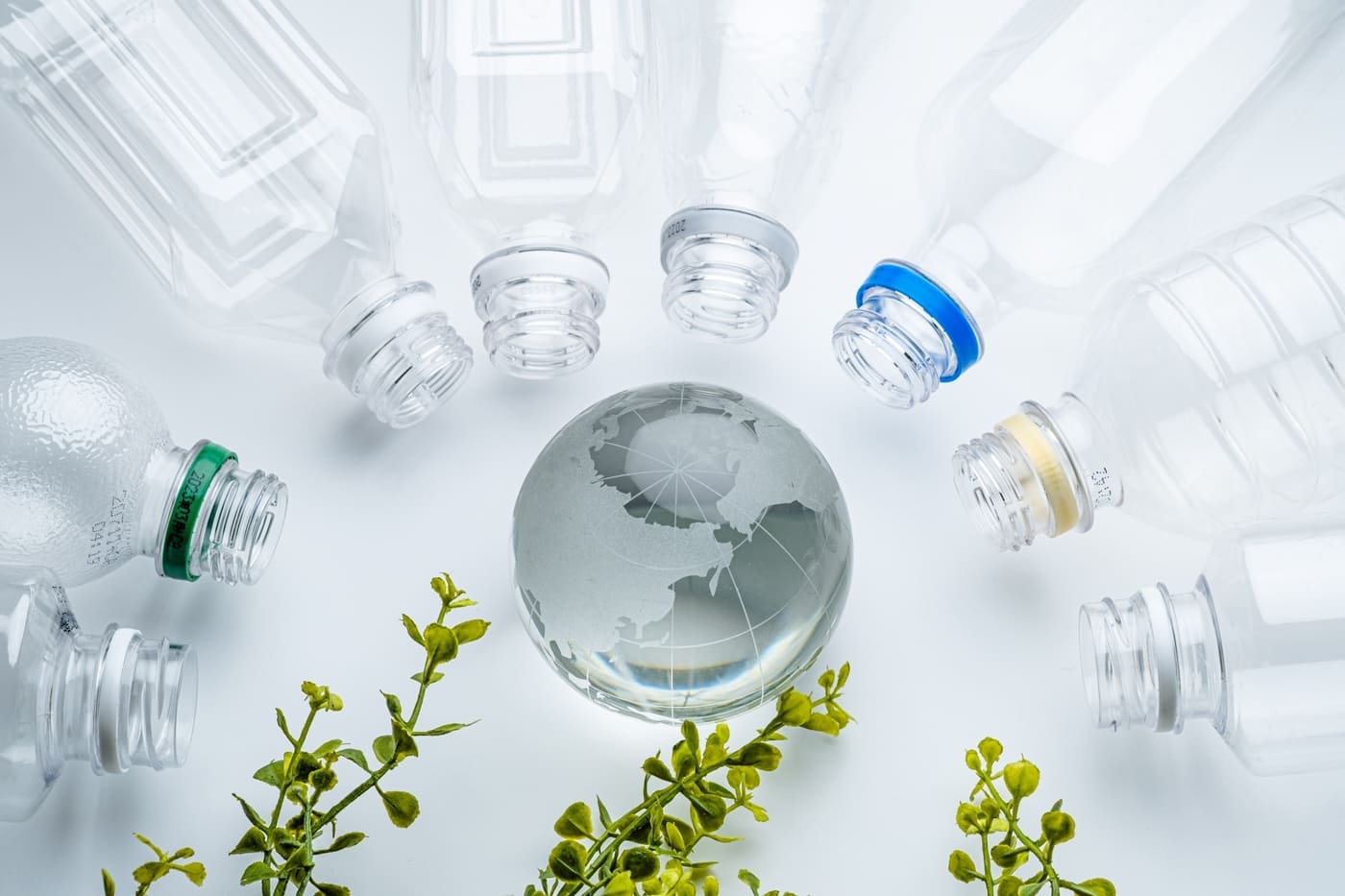 地球を囲むようにペットボトルとグリーンが置かれていて、生分解性プラスチックを表現しているイメージ画像