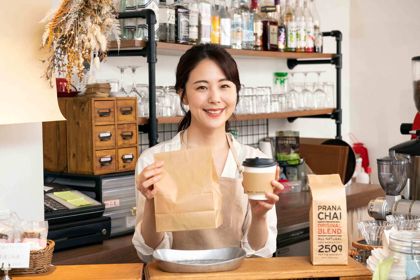 カフェのようなお店でドリンクを提供する笑顔の女性スタッフ