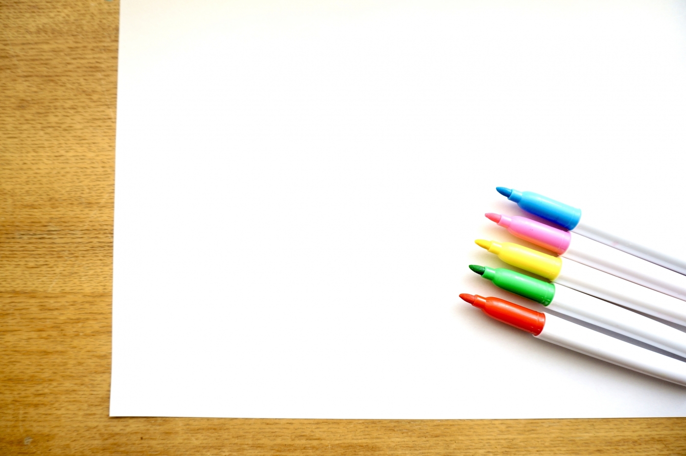 手描きPOPの作成のために用意された白い大きい紙と赤緑黄桃青の5色のサインペン