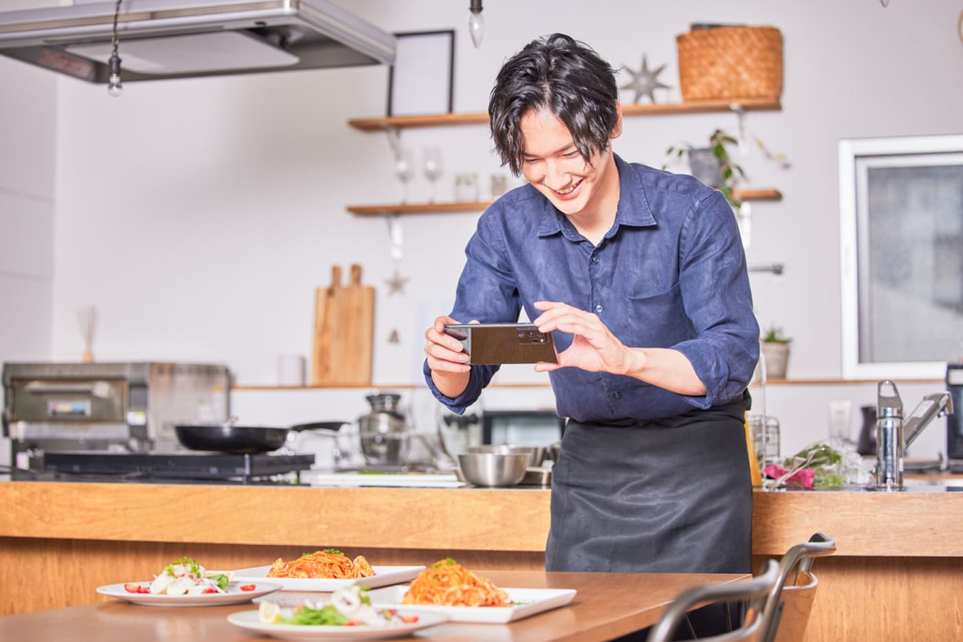 男性スタッフが料理店の店内で楽しそうにスマートフォンを使って料理の写真を撮影している場面