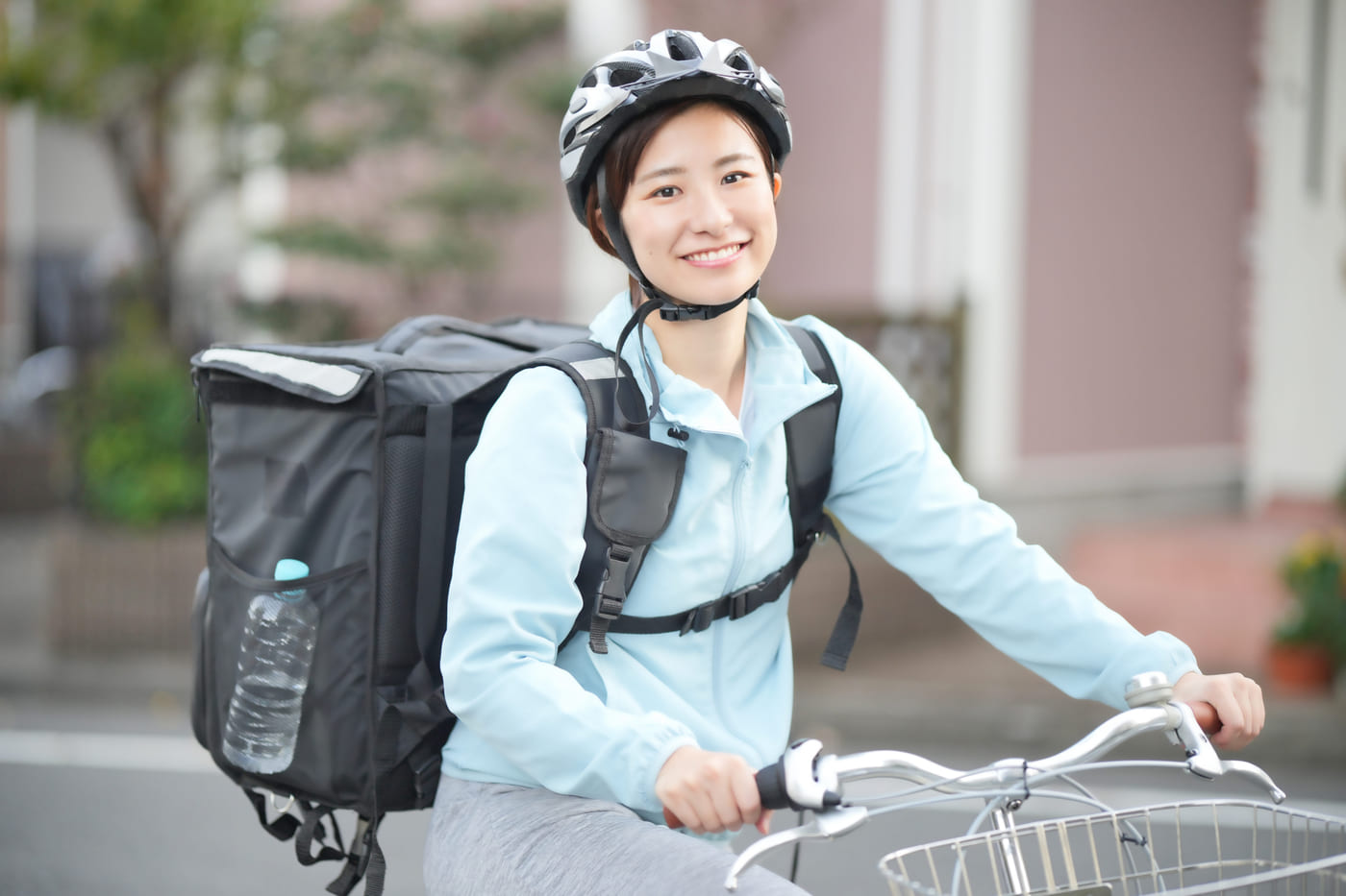 配達用のバッグを背負って自転車に乗るフードデリバリーの女性